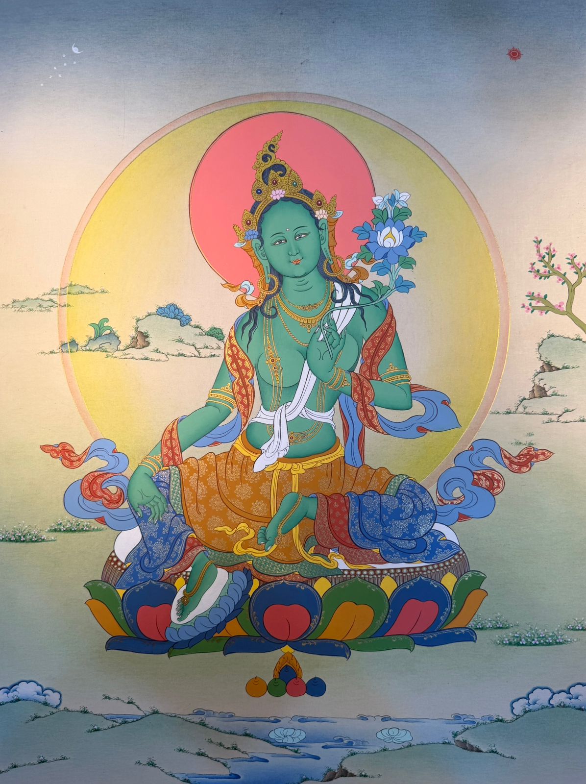 Thangka painting of Green Tara seated on a lotus with blue and orange robes