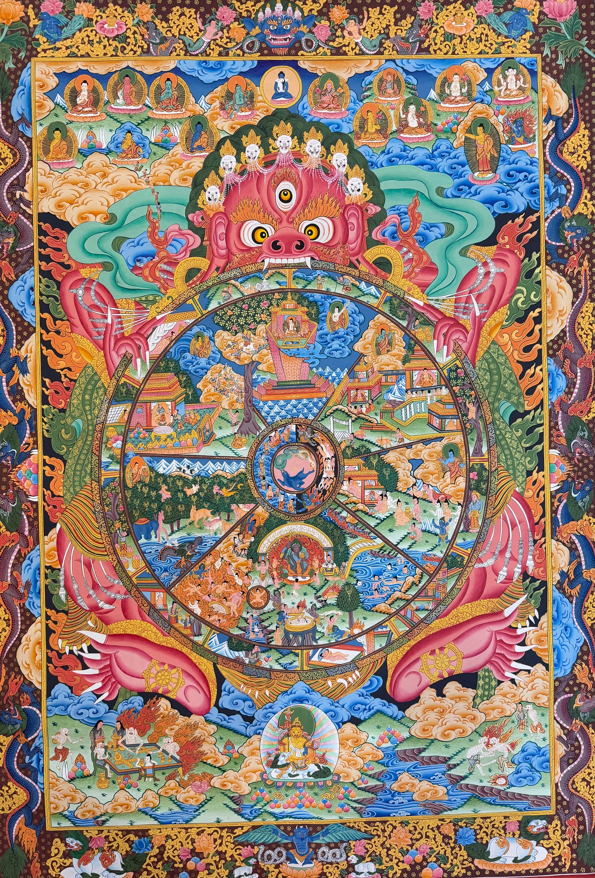 Thangka painting with central circular wheel, pink guardian face, detailed deities and ornate border
