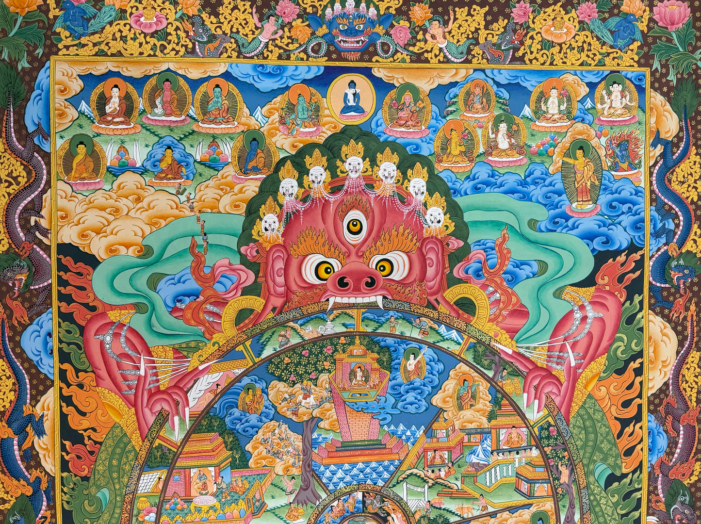 Thangka painting with seated figures along the top, pink guardian face, and central circular wheel