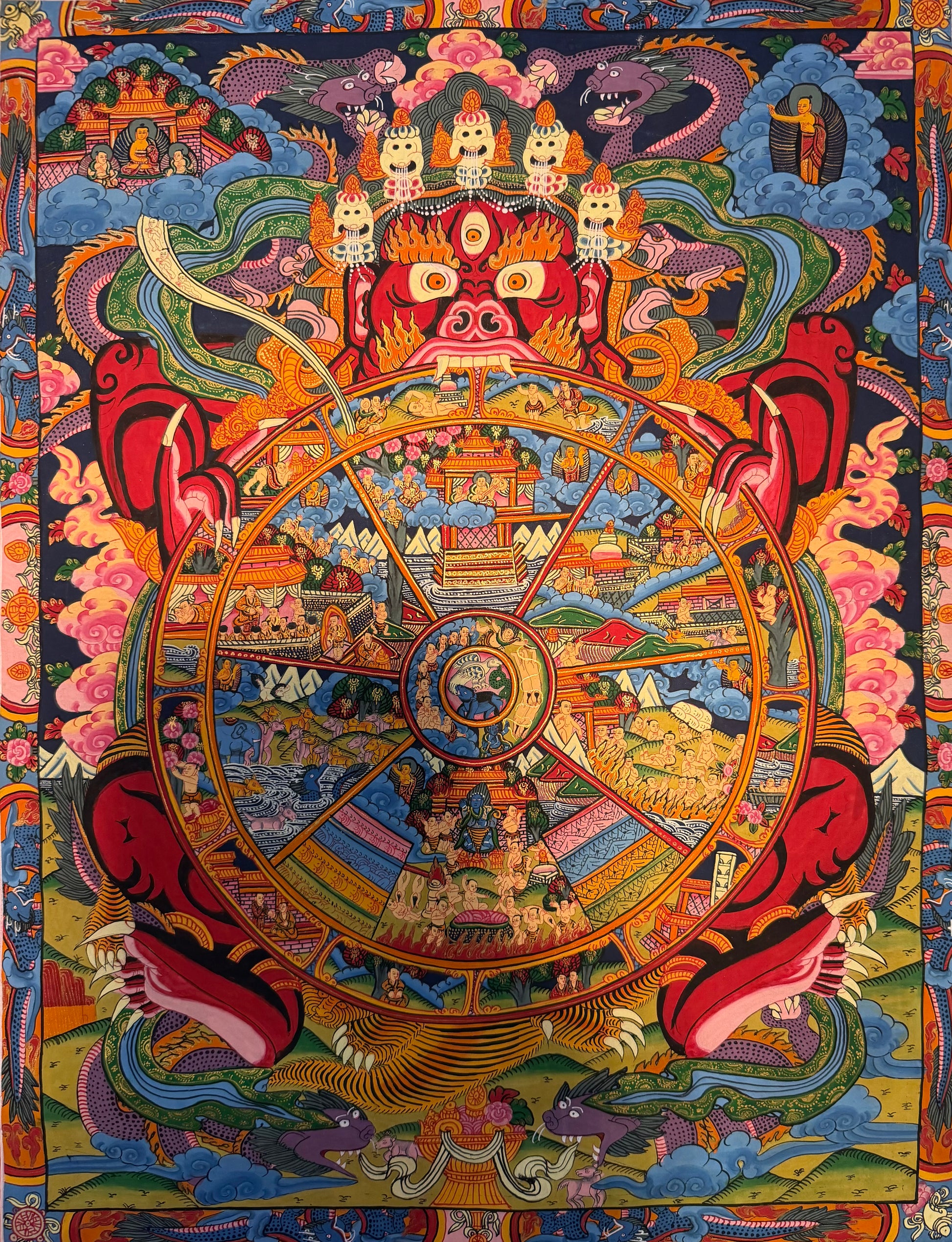 Thangka painting with ornate circular wheel, central deity faces, and vivid scenes