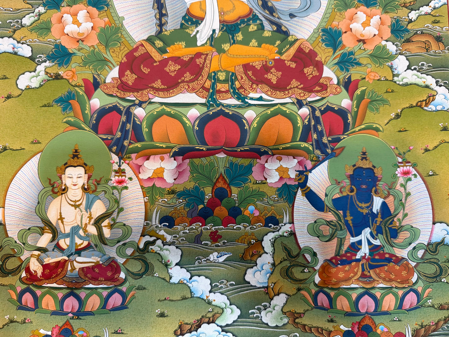 Thangka painting with three seated deities, floral details, and cloud and landscape motifs
