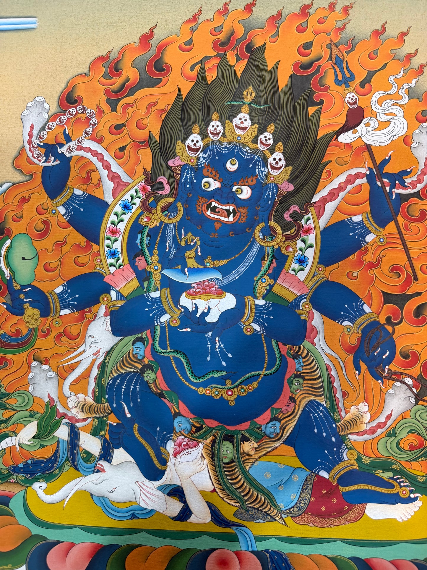 Mahakala thangka painting: close portrait of blue deity, flaming backdrop, ornate jewelry, skulls